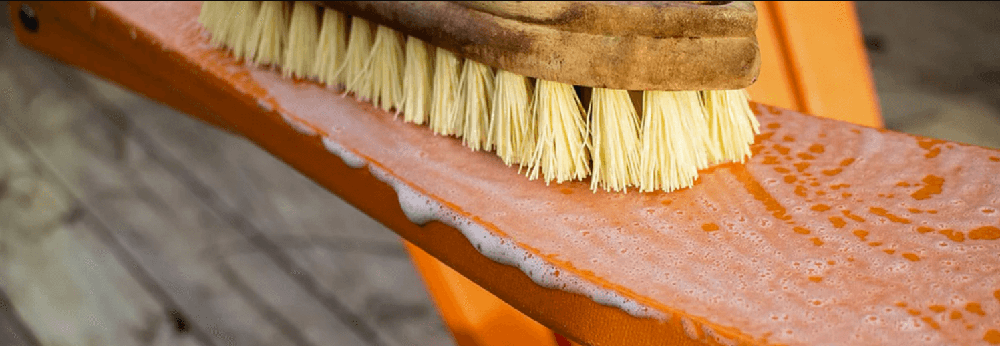 Scrubbing orange outdoor furniture with a brush and soapy water to clean before storage.